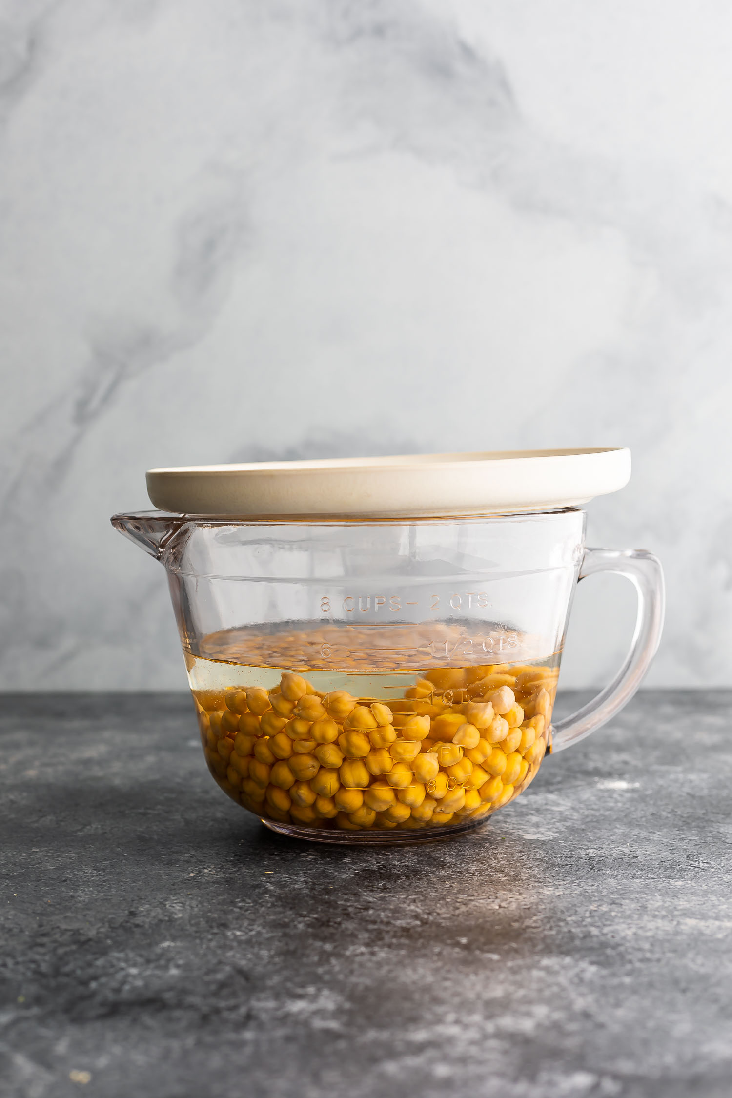 dried chickpeas soaking in large measuring cup, covered with a plate