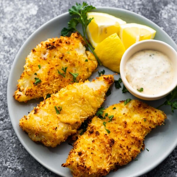 crispy air fryer fish on plate with lemon wedges and tartar sauce
