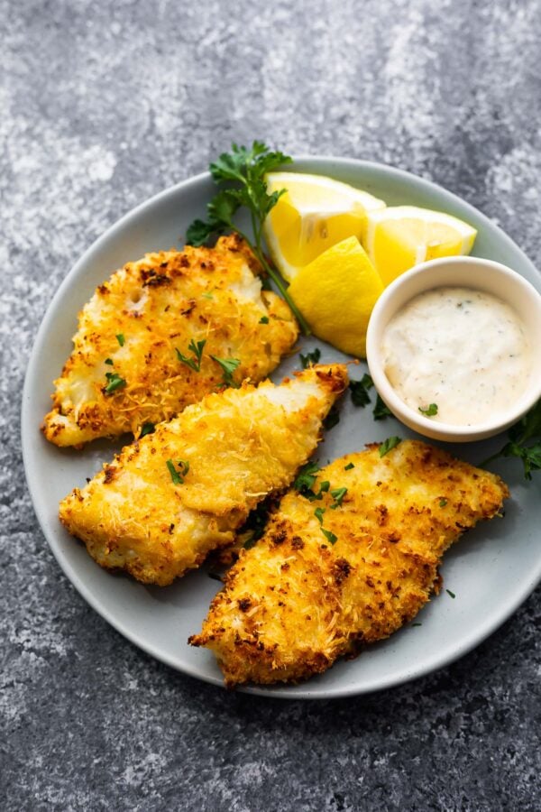 crispy air fryer fish on plate with lemon wedges and tartar sauce