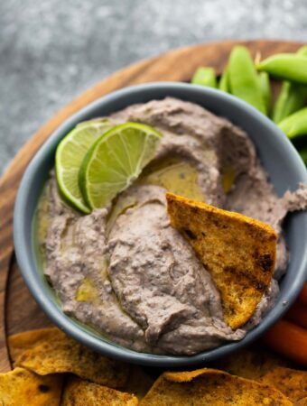 pita chip in bowl of black bean hummus showing creamy texture