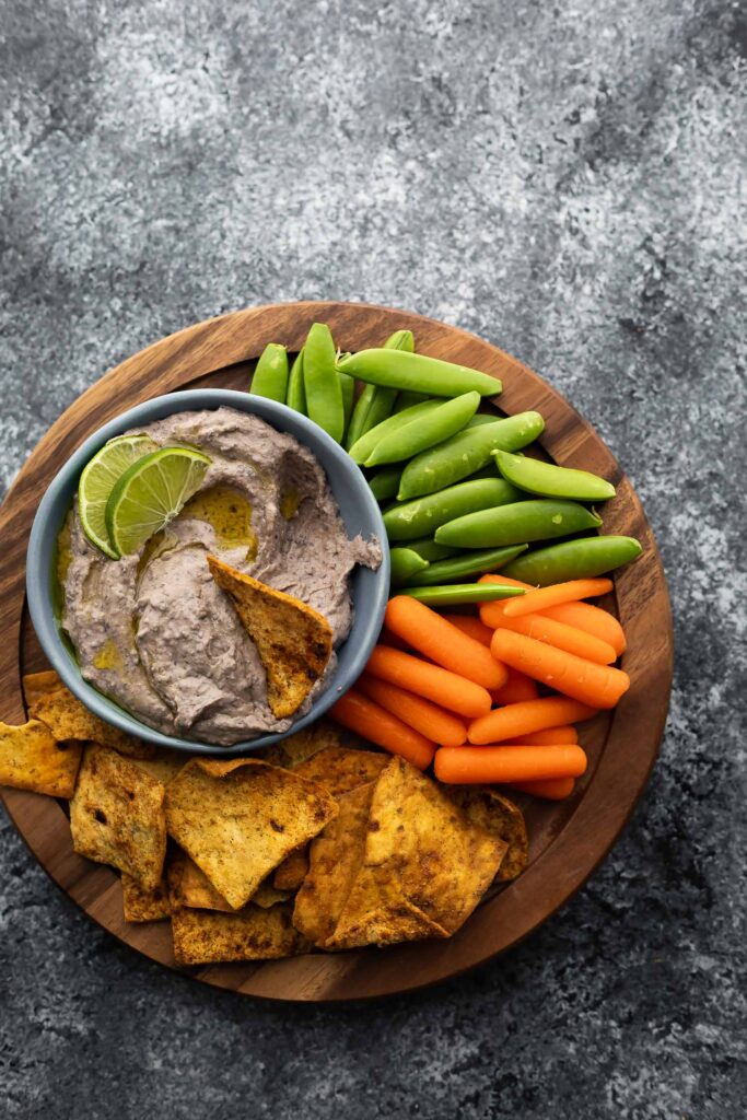 overhead view of a platter with carrots, peas, pita chips and black bean hummus
