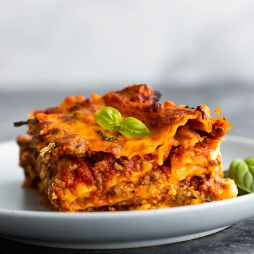 side angle view of slice of lasagna on plate topped with basil