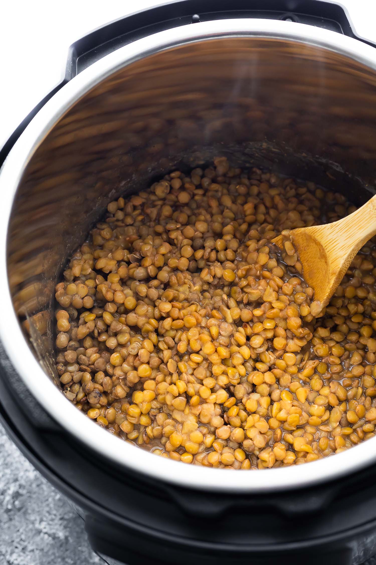 close up of green lentils in instant pot with wooden spoon