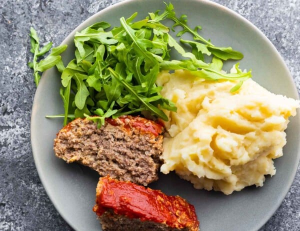 plate with two slices of meatloaf, arugula, and mashed potatoes