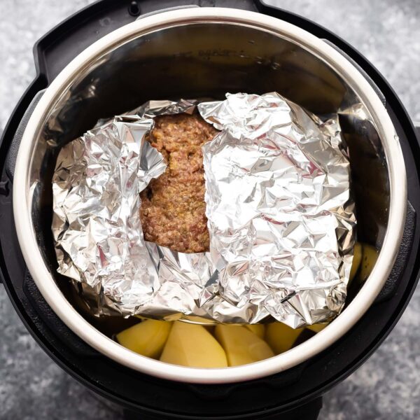 uncooked meatloaf wrapped in foil on a trivet placed over potatoes in the instant pot