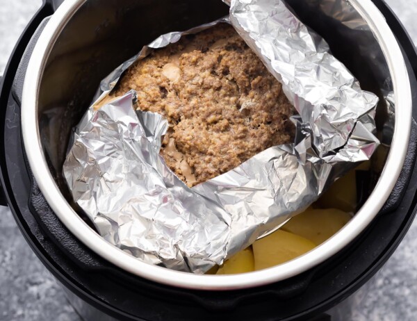 meatloaf wrapped in foil on trivet over potatoes in instant pot after cooking through