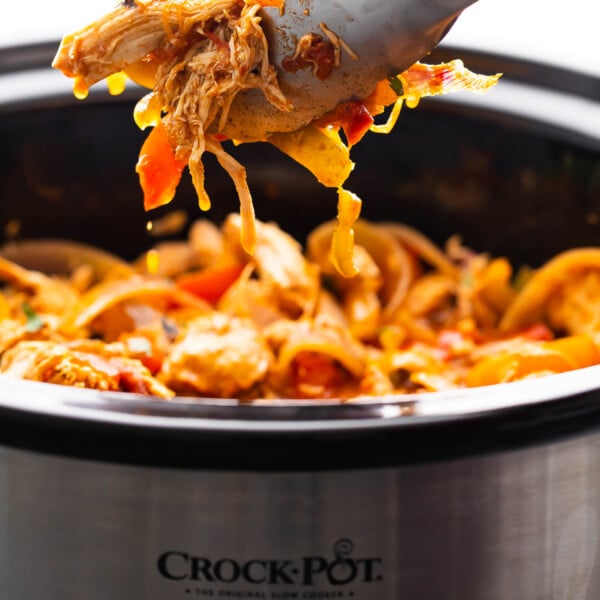 tongs lifting slow cooker chicken fajitas out of the slow cooker