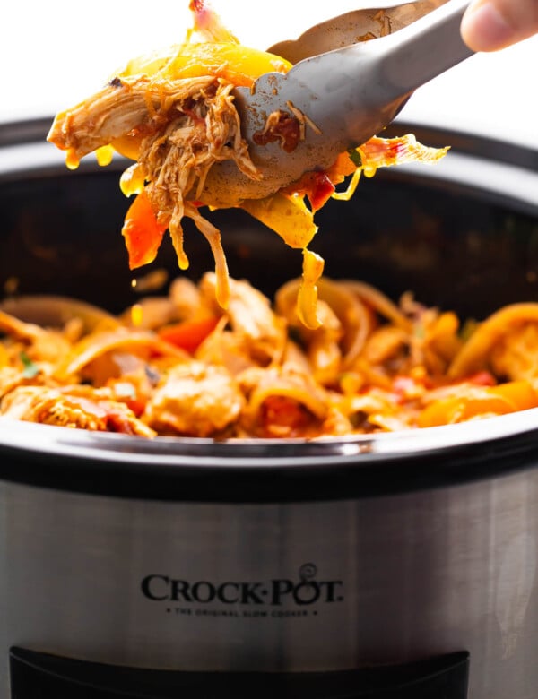 tongs lifting slow cooker chicken fajitas out of the slow cooker