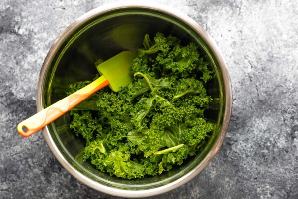 kale tossed in oil in a bowl with spatula