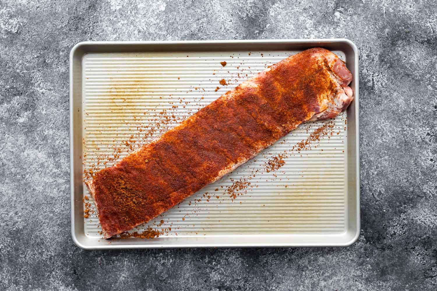 rack of ribs coated in dry rub on baking sheet