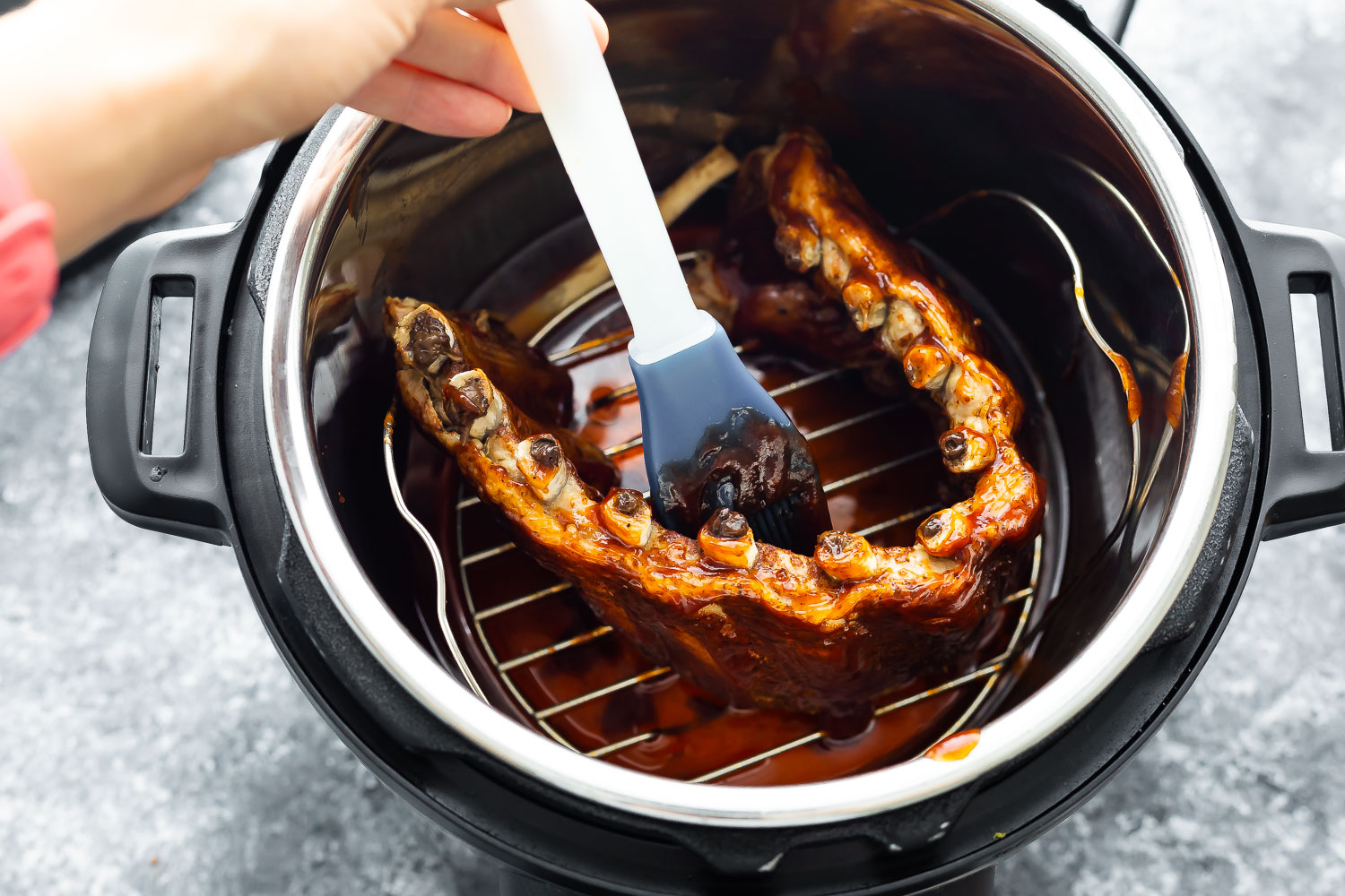 cooked ribs in instant pot being brushed with bbq sauce using silicone brush