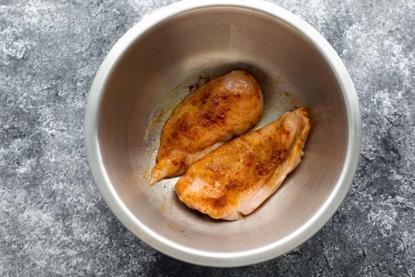chicken breasts in silver bowl tossed in seasonings