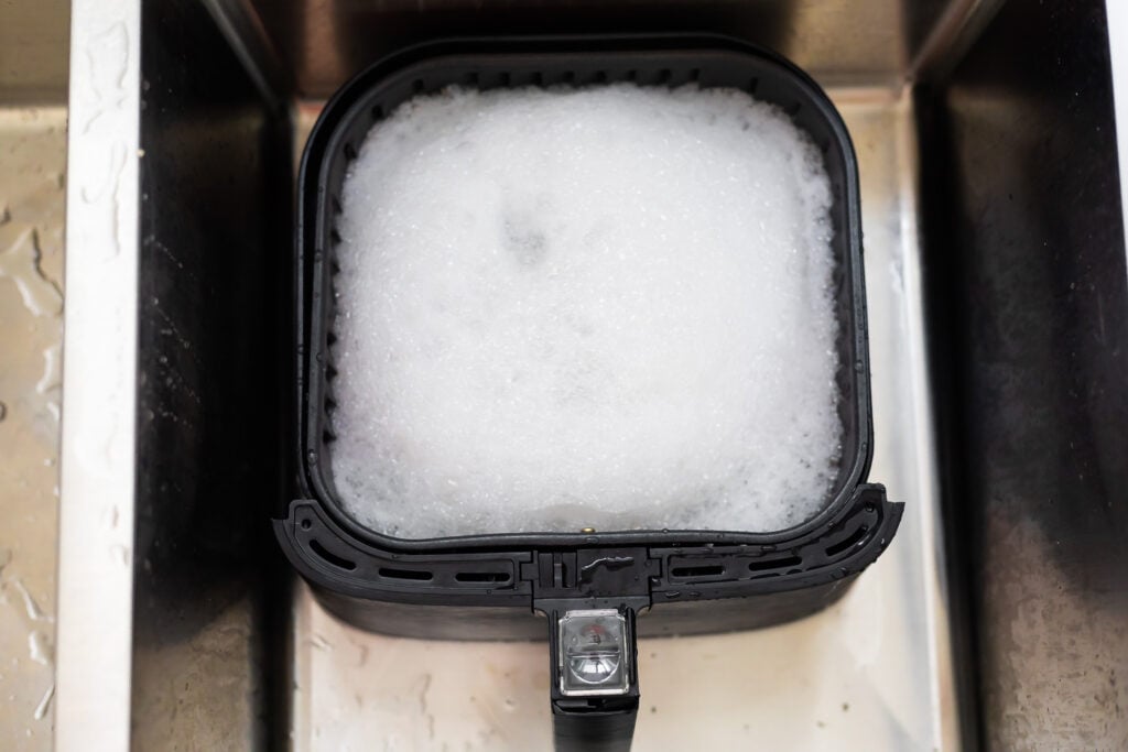 air fryer basket soaking in the sink with soapy water