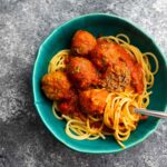 bowl of spaghetti and meatballs with one meatball broken open and spaghetti wound around a fork