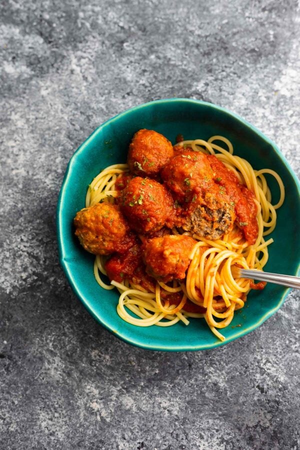 bowl of spaghetti and meatballs with one meatball broken open and spaghetti wound around a fork