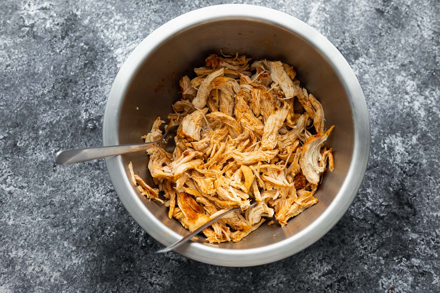overhead view of shredded chicken in bowl with two forks