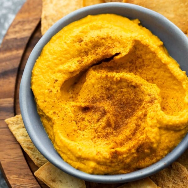 close up view of pumpkin hummus in blue bowl with pita chip dipping in