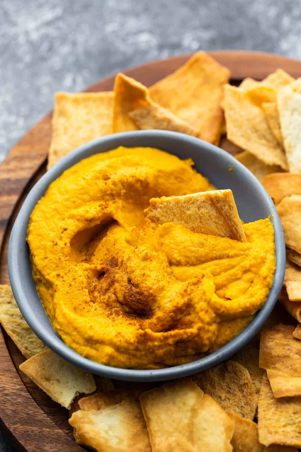 close up view of pumpkin hummus in blue bowl with pita chip dipping in