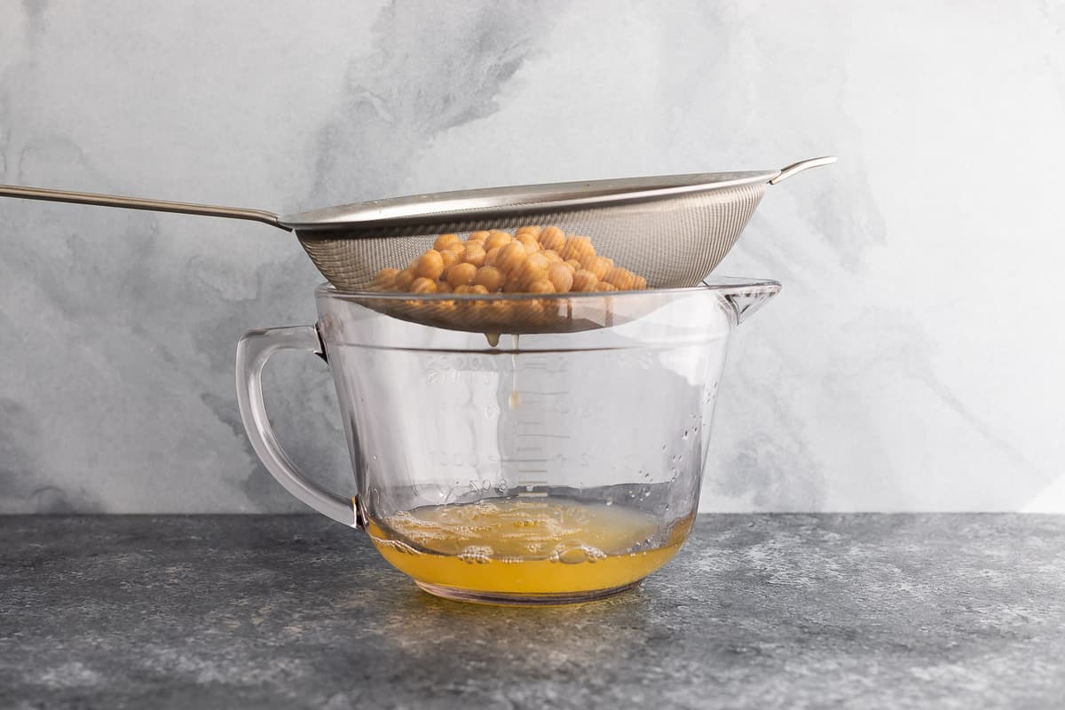 chickpea liquid straining through mesh strainer into large glass measuring cup