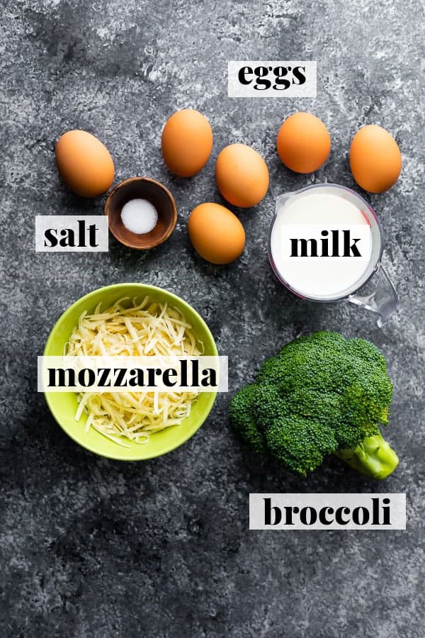 ingredients on grey surface from above including eggs, milk, salt, mozarella, and broccoli