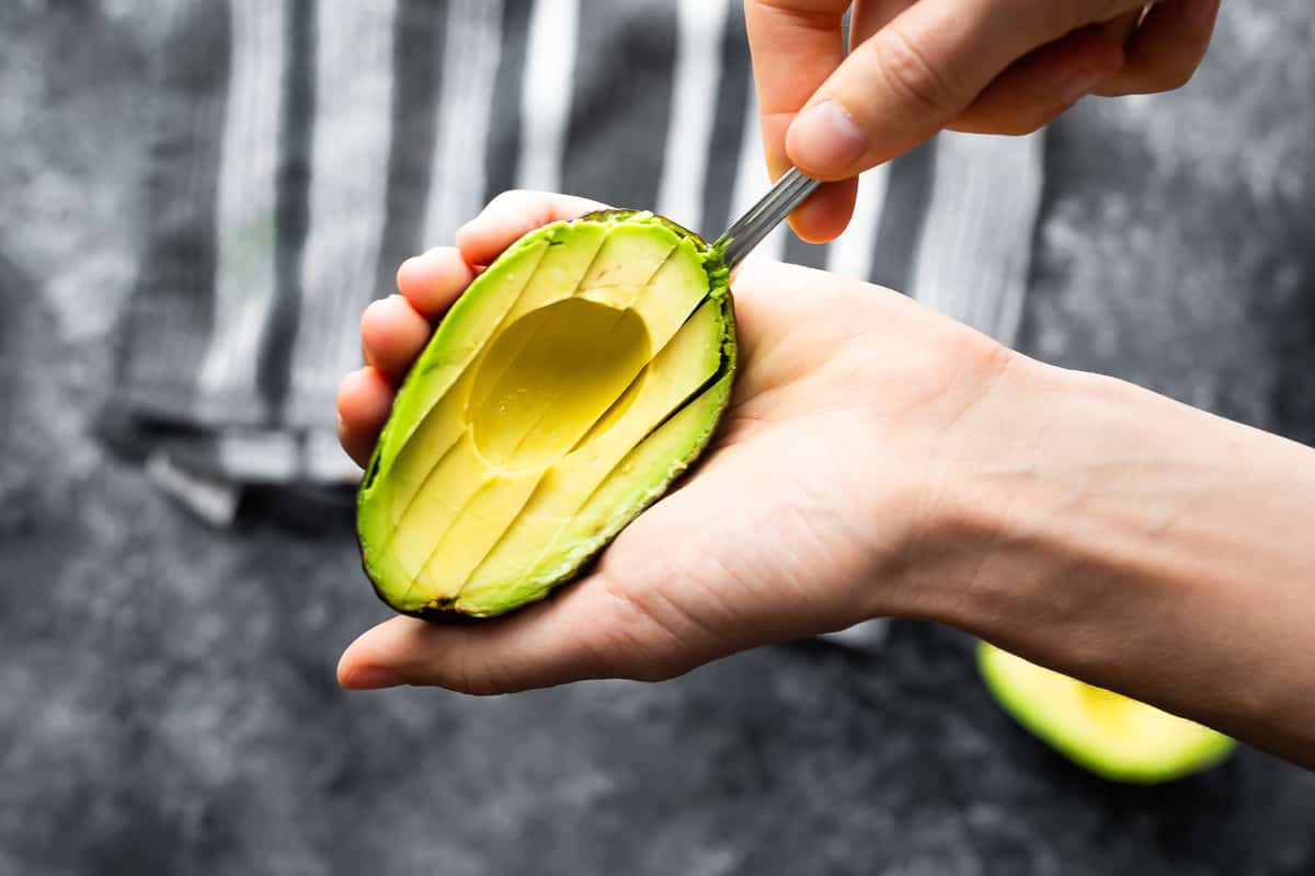 scooping sliced avocado out of the skin with a spoon