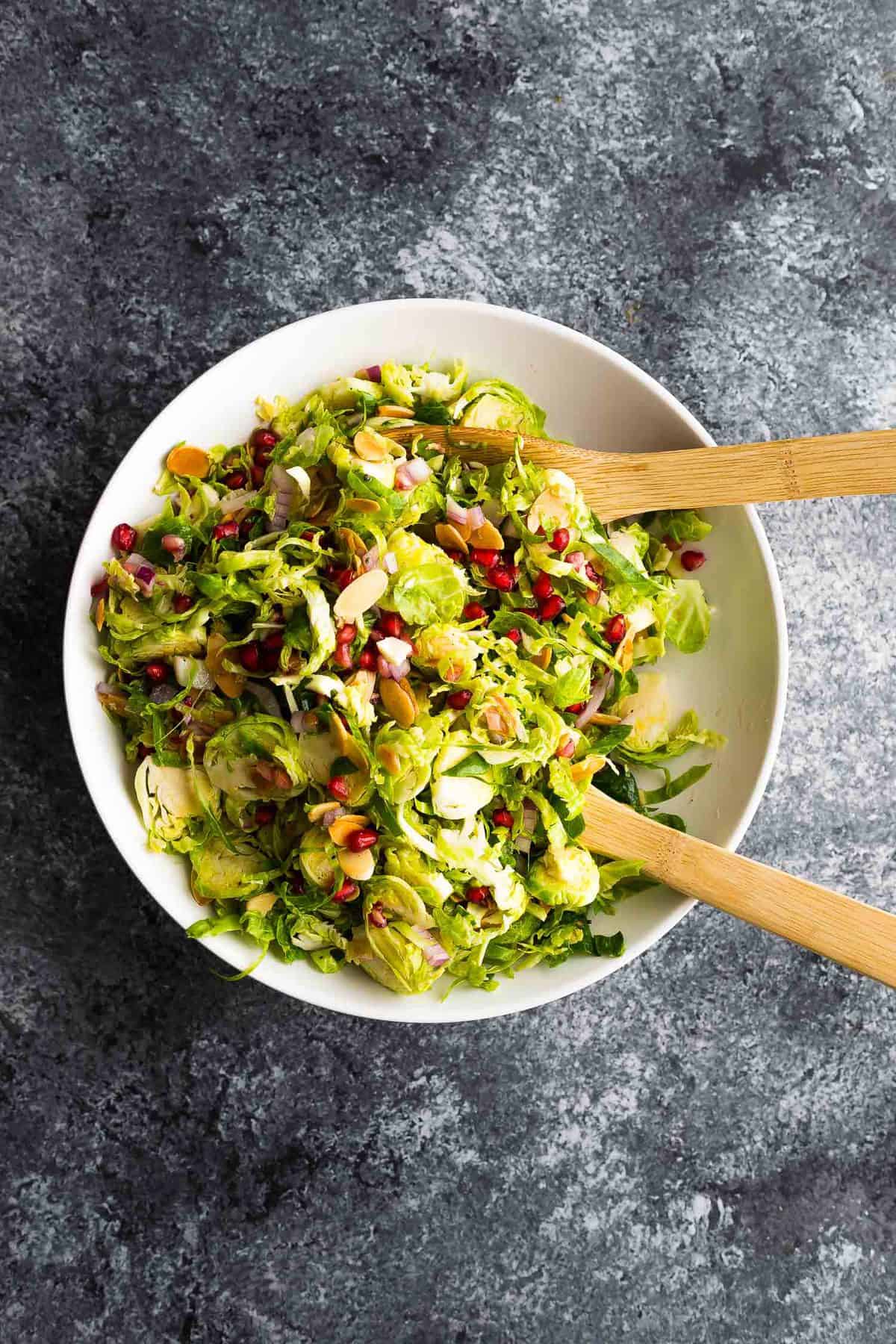 pomegranate brussels sprouts salad in white bowl with salad spoons