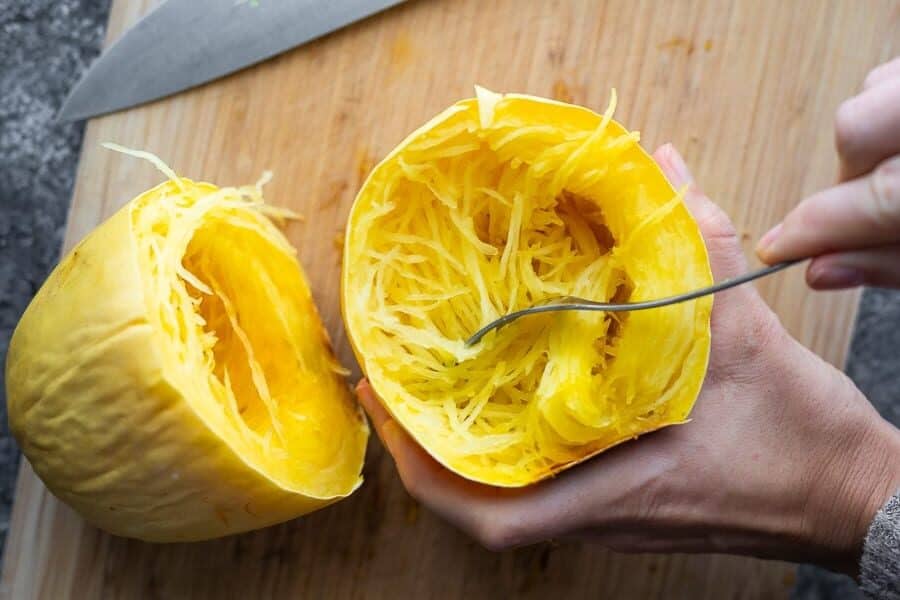 hand holding half a cooked spaghetti squash and scooping out the insides with a fork