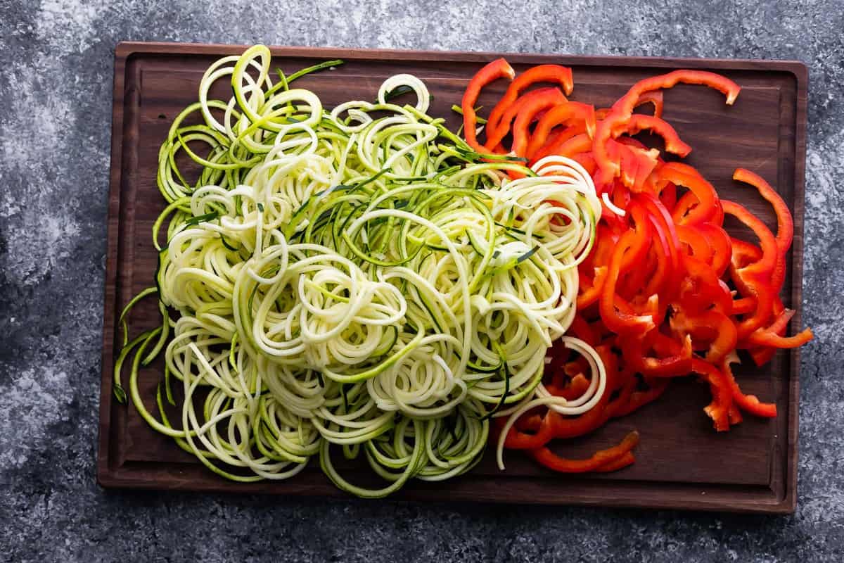 spiralized zucchini and sliced red peppers on cutting board