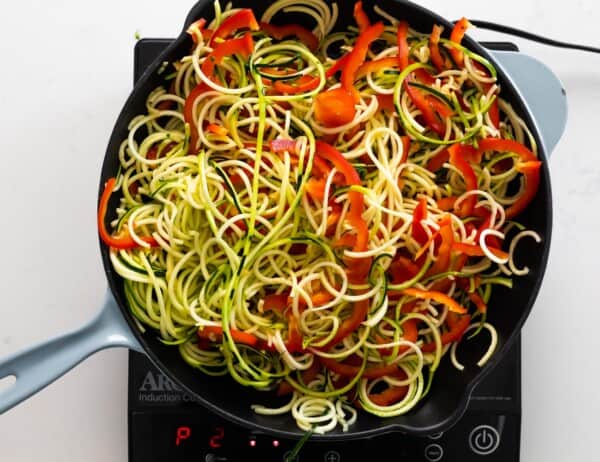 cooking zucchini noodles and sliced red pepper in frying pan