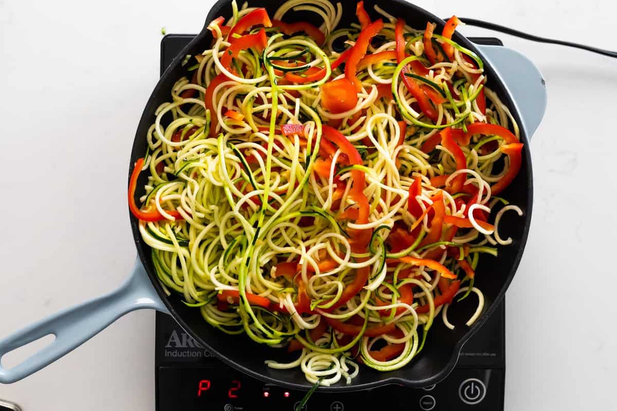 cooking zucchini noodles and sliced red pepper in frying pan