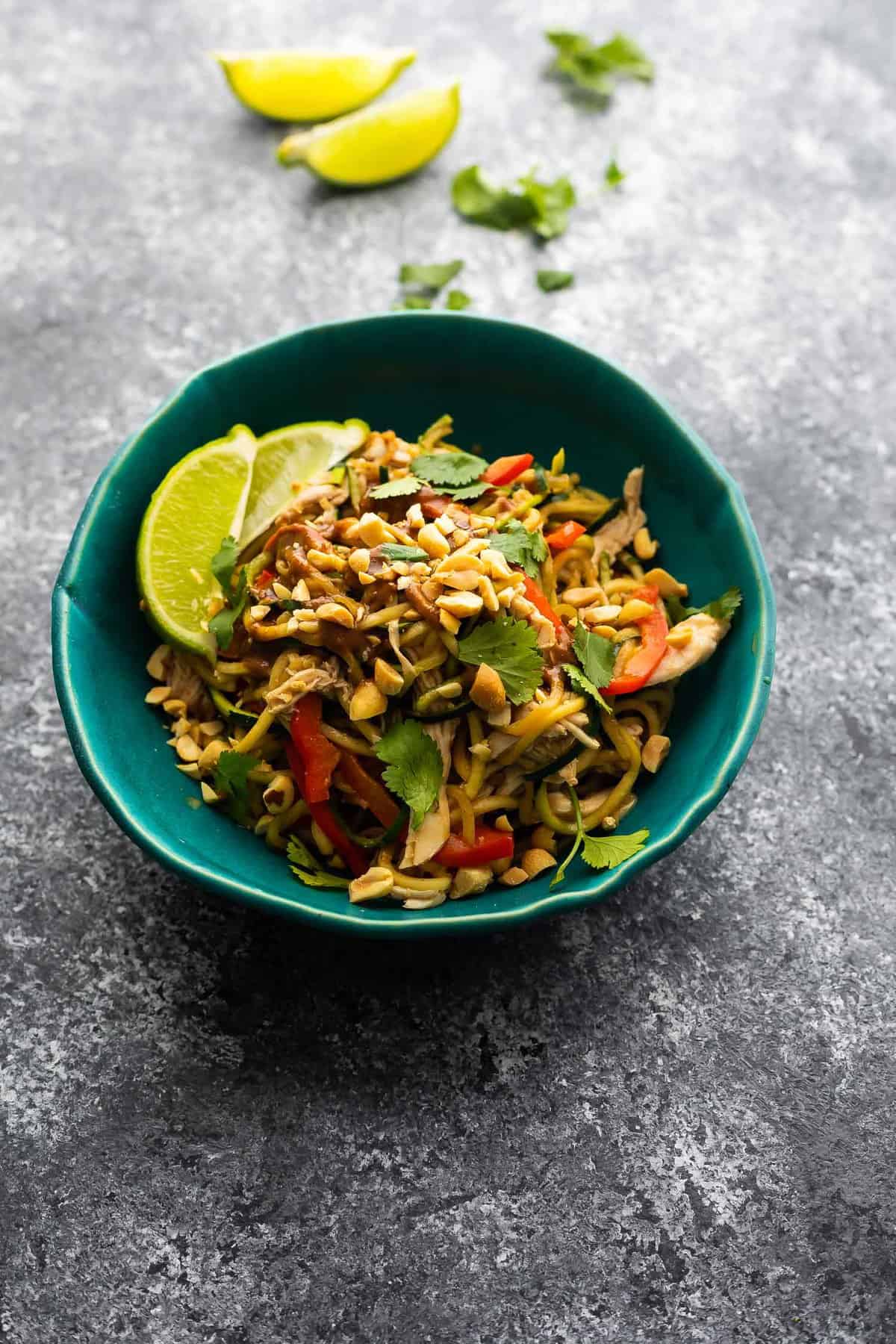 peanut chicken zucchini noodles in blue bowl with lime wedges