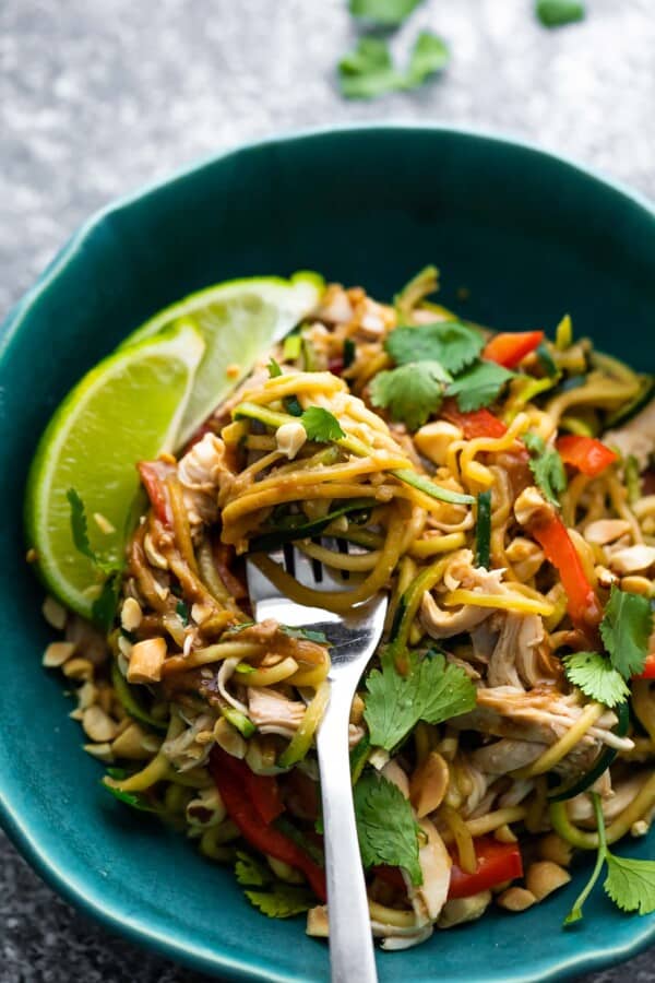 close up peanut chicken zucchini noodles in blue bowl with lime wedges