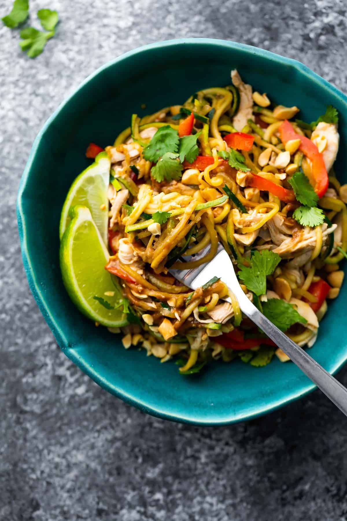 overhead peanut chicken zucchini noodles in blue bowl with lime wedges