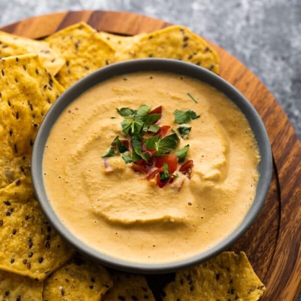 bowl of cashew queso topped with tomatoes and cilantro surrounded by chips