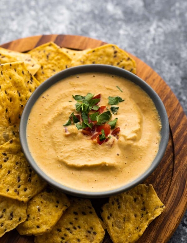 bowl of cashew queso topped with tomatoes and cilantro surrounded by chips