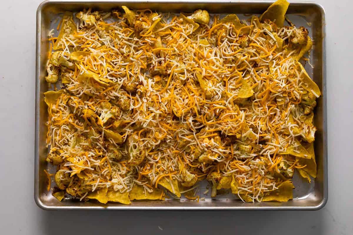 cauliflower nachos on sheetpan topped with shredded cheese