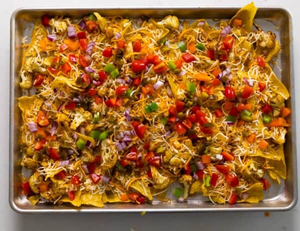 cauliflower nachos on sheetpan topped with all toppings (bell peppers, red onion, jalapeno and tomatoes)