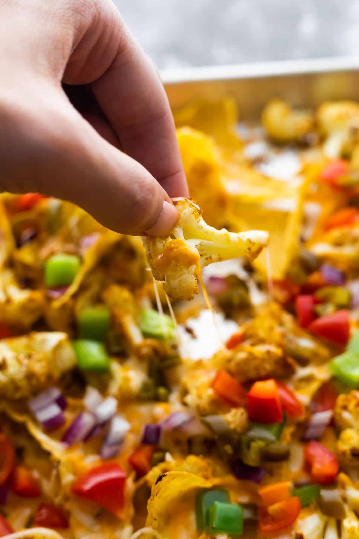 pulling a cheesy cauliflower 'nacho' from the pan