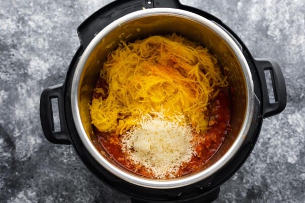 adding spaghetti squash noodles and parmesan cheese to meatsauce in instant pot