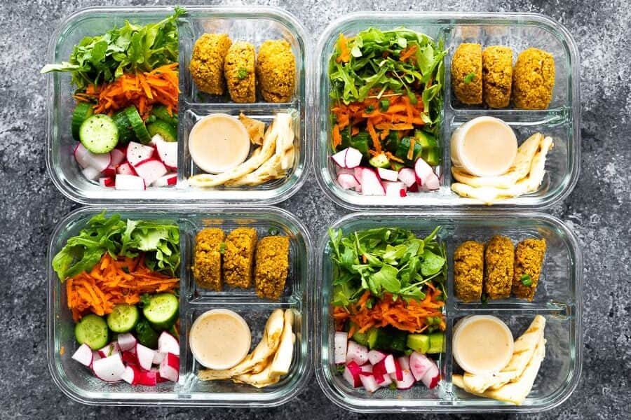 overhead shot of a falafel in meal prep containers with salad, dressing, and veggies portioned out 