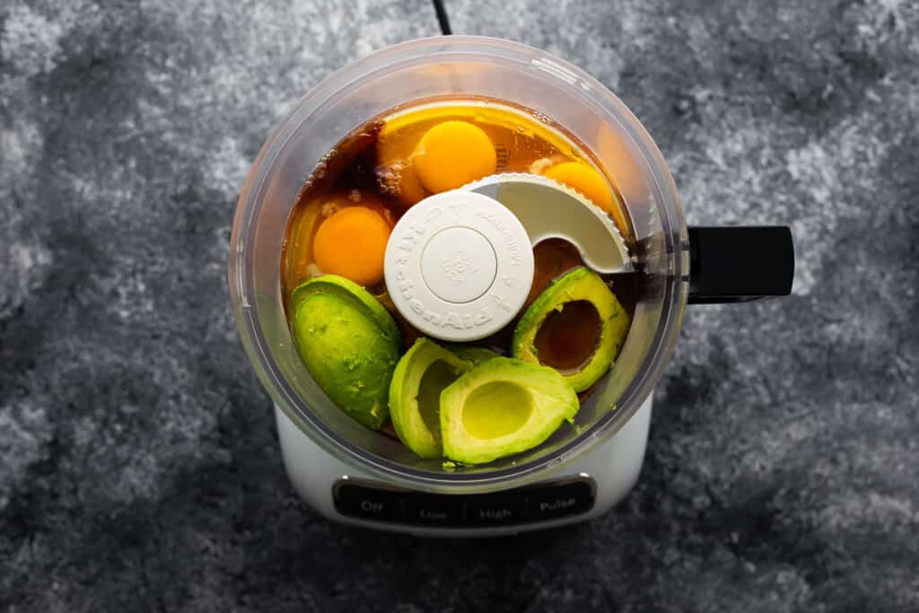 Adding avocado, eggs, maple syrup and vanilla extract to the food processor.