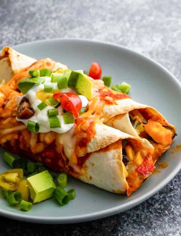 A plate of vegetarian enchiladas topped with avocado and sour cream