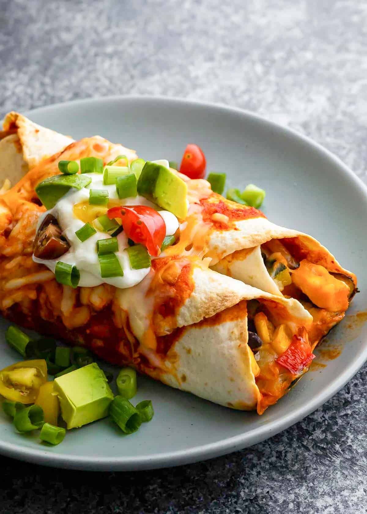 A plate of vegetarian enchiladas topped with avocado and sour cream