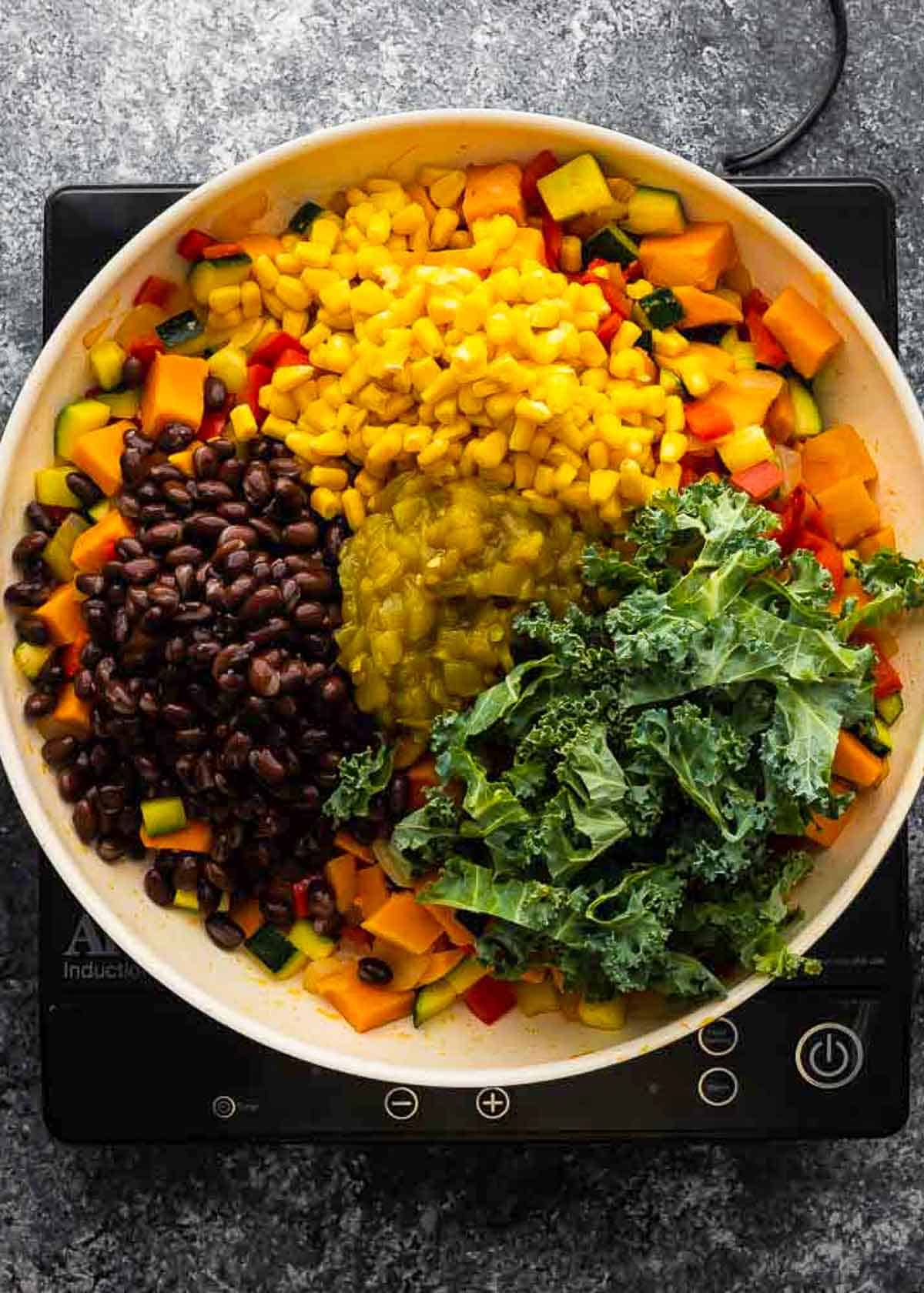 cooked vegetables, black beans, corn and kale in a large skillet