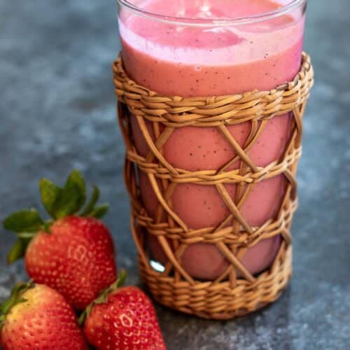 a closeup shot of passionfruit smoothie in a cup with strawberries on the side.