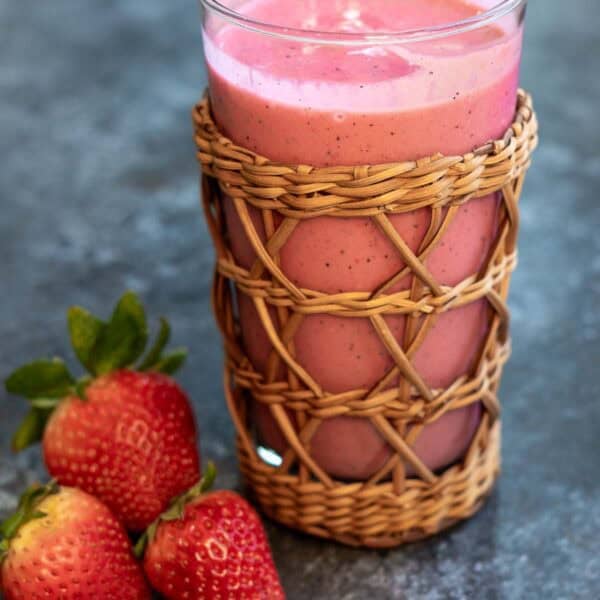 a closeup shot of passionfruit smoothie in a cup with strawberries on the side.