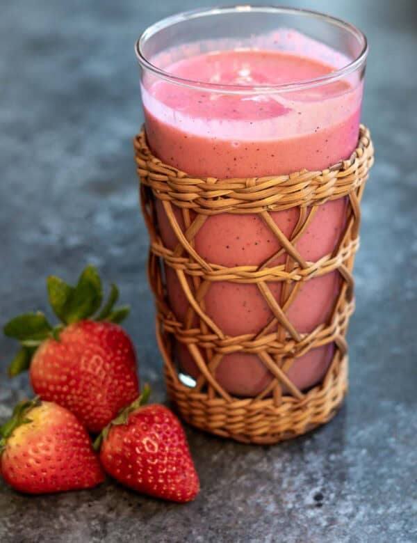 a closeup shot of passionfruit smoothie in a cup with strawberries on the side.