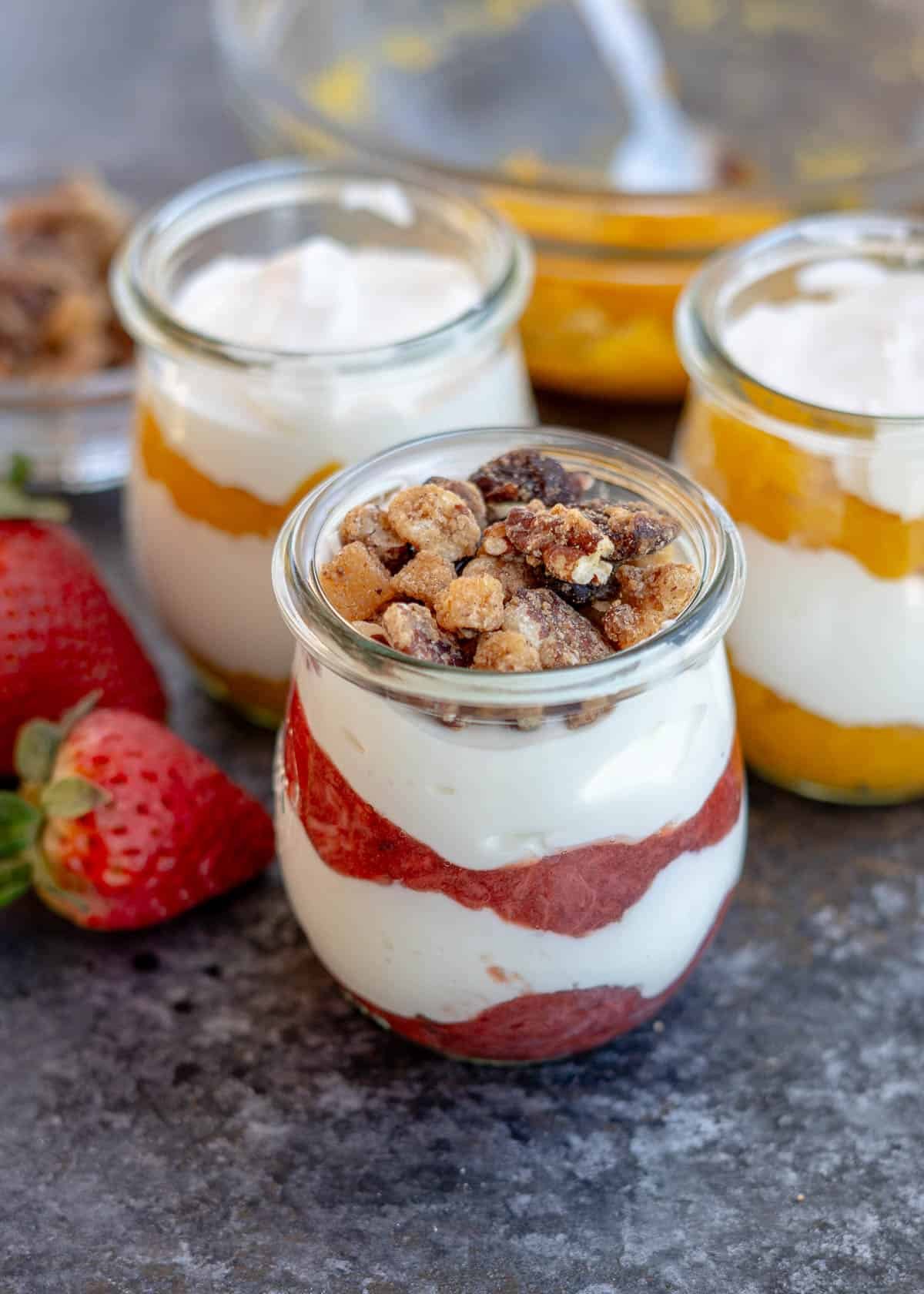 strawberry yogurt parfait topped with granola; two jars of mango yogurt parfaits behind.