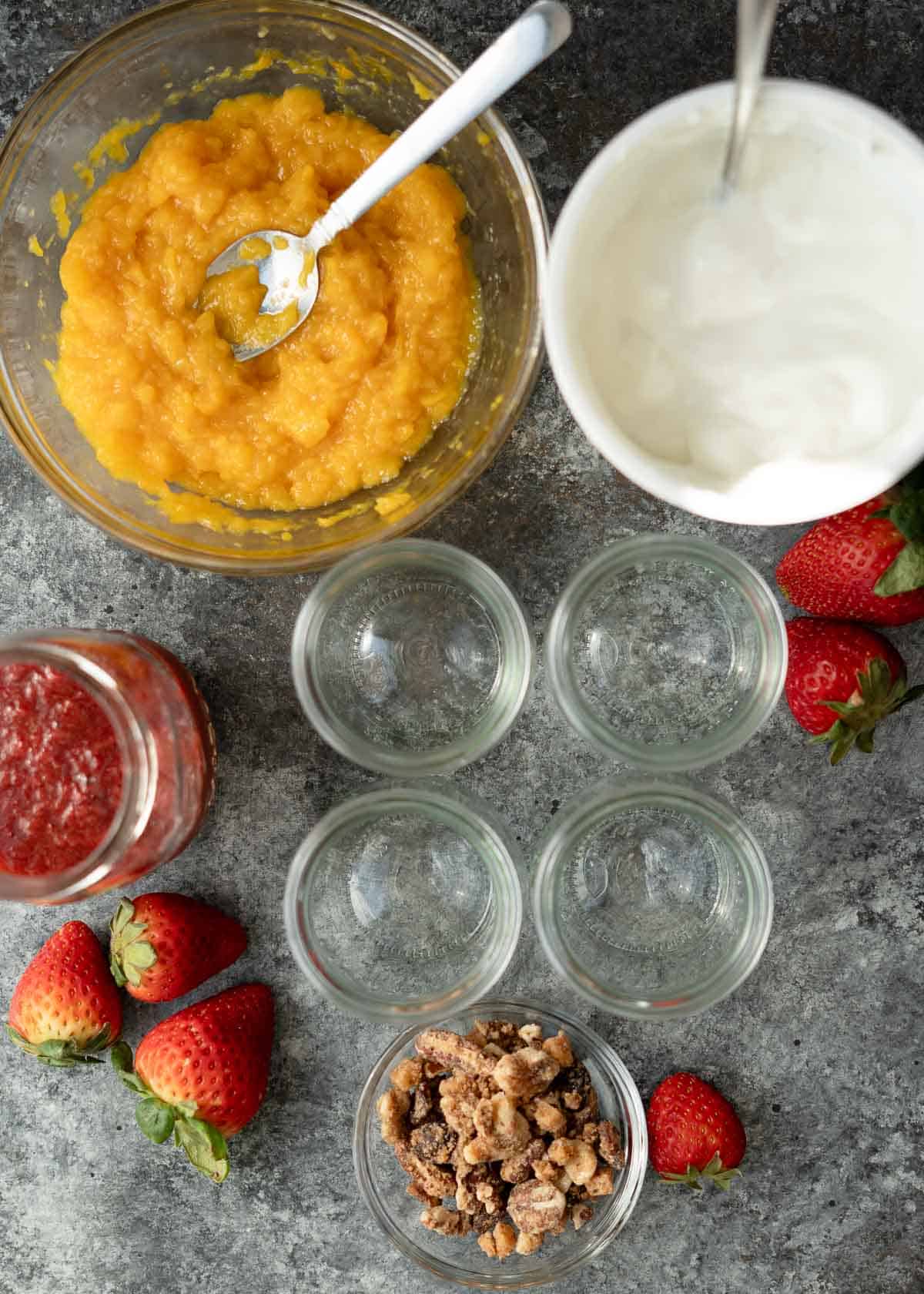 fruit sauce, yogurt, and granola surrounding empty jars for high-protein parfaits