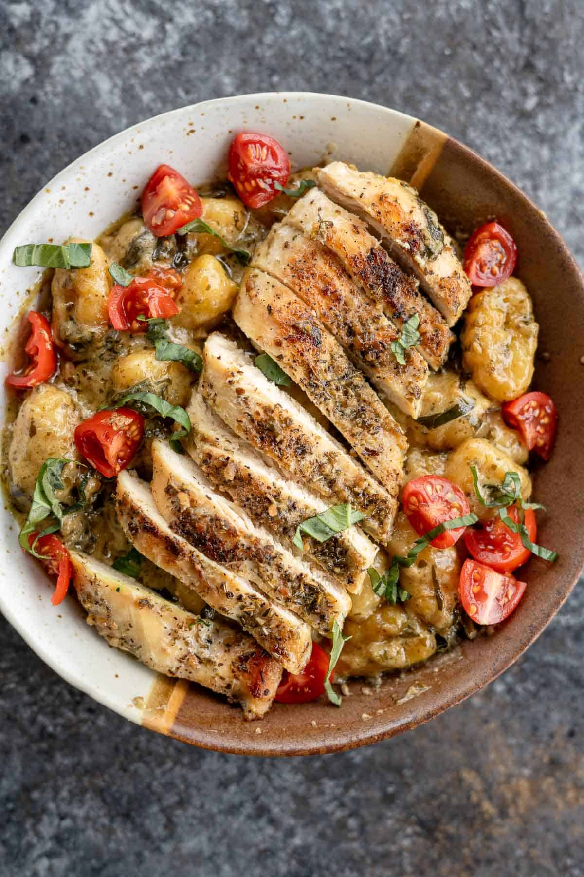 An overhead shot of pesto gnocchi in a bowl with sliced chicken